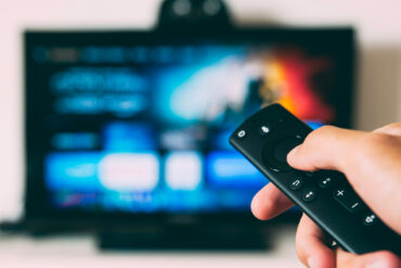 télécommande en premier plan, en fond une télévision flou qui est sur un service de streaming pour voir un documentaire