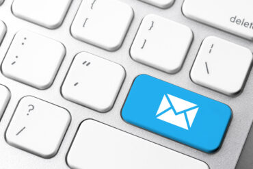 clavier d'ordinateur blanc et argent ou la touche entrée a été remplacée par une touche avec une enveloppe signifiant "e-mail". La touche est bleu cyan