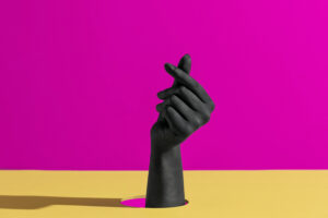 against a colorful background, yellow and mauve, with a hand, painted black, emerging from the scene.
